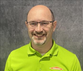 Male owner in lime green SERVPRO shirt standing in front of grey backdrop