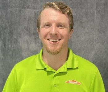 Male employee standing in front of grey backdrop with lime green SERVPRO shirt on