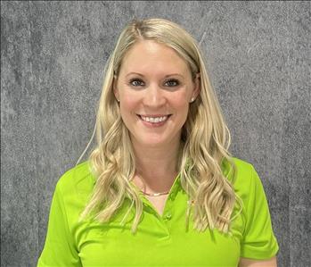 Blonde female wearing lime green SERVPRO shirt standing in front of grey backdrop